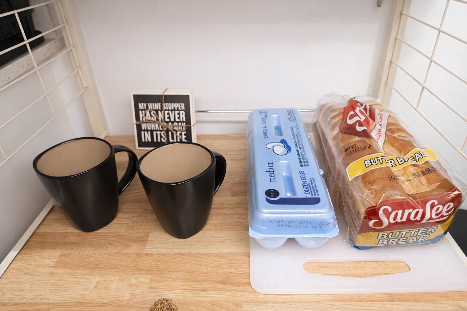 A kitchen counter with two black mugs, a carton of medium eggs, and a package of Sara Lee butter bread.