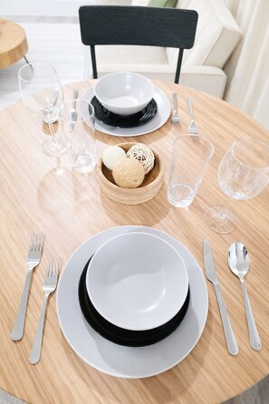 Une table de salle à manger ronde, avec une assiette blanche et noire, des couverts en argent et des verres transparents.