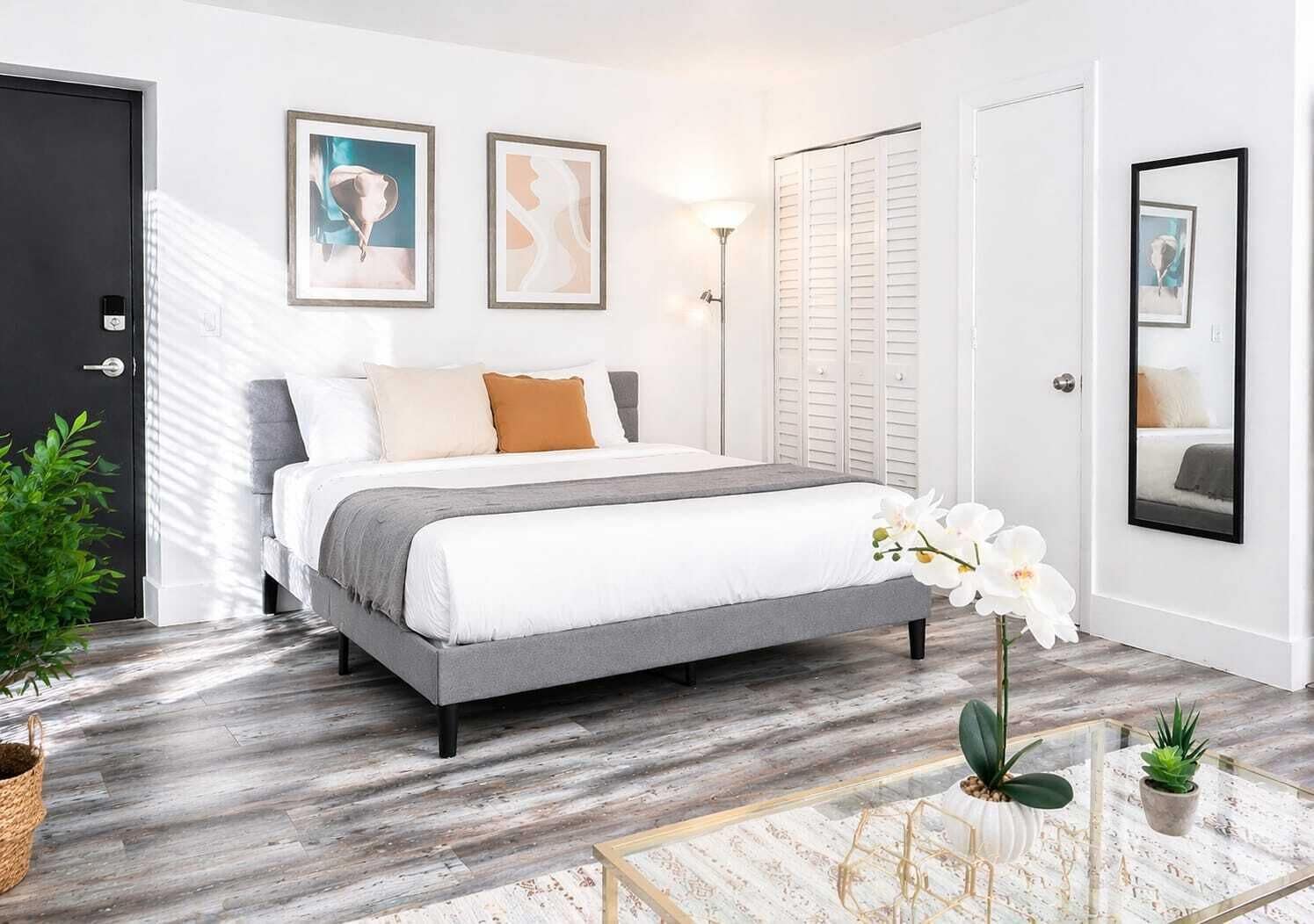 Une chambre à coucher moderne, avec un lit, des tables de chevet, un miroir et des œuvres d’art accrochées aux murs.