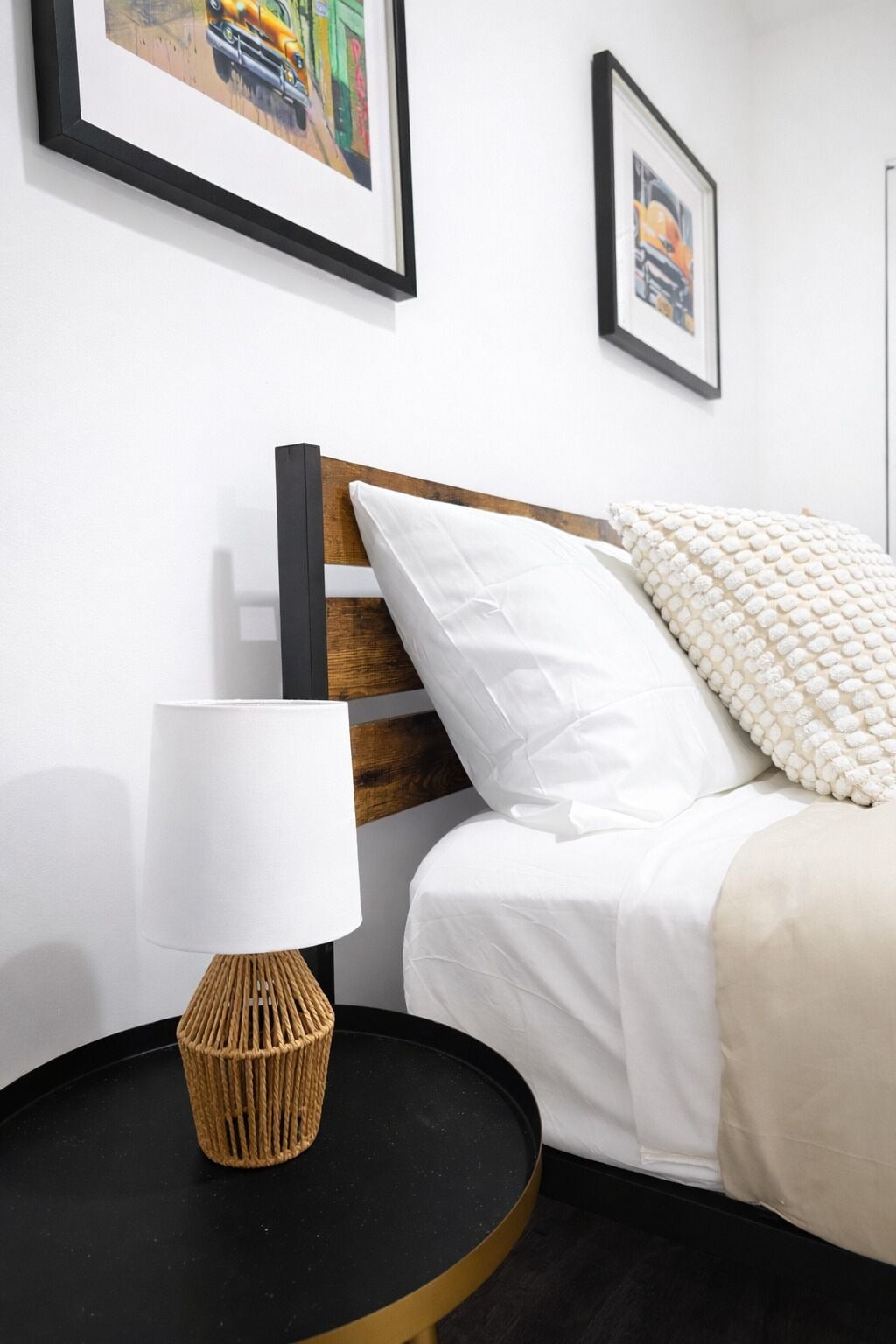 Une chambre à coucher bien rangée, avec un lit, une table de chevet dotée d’une lampe et des œuvres d’art encadrées accrochées au mur.
