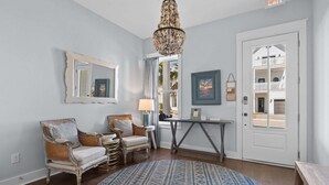 A room with a round blue rug, two wicker chairs, a wooden bench, a table, a mirror, and a chandelier. - The Lazy Yorkie | Family Beach Getaway | Sleeps 10 | Great Rates (Inlet Beach)
