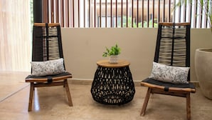 Two wicker chairs with black and white cushions, a round wooden table with a potted plant, and a large planter. - Paravian 704 2BR Condo Playa del Carmen (Playa del Carmen)