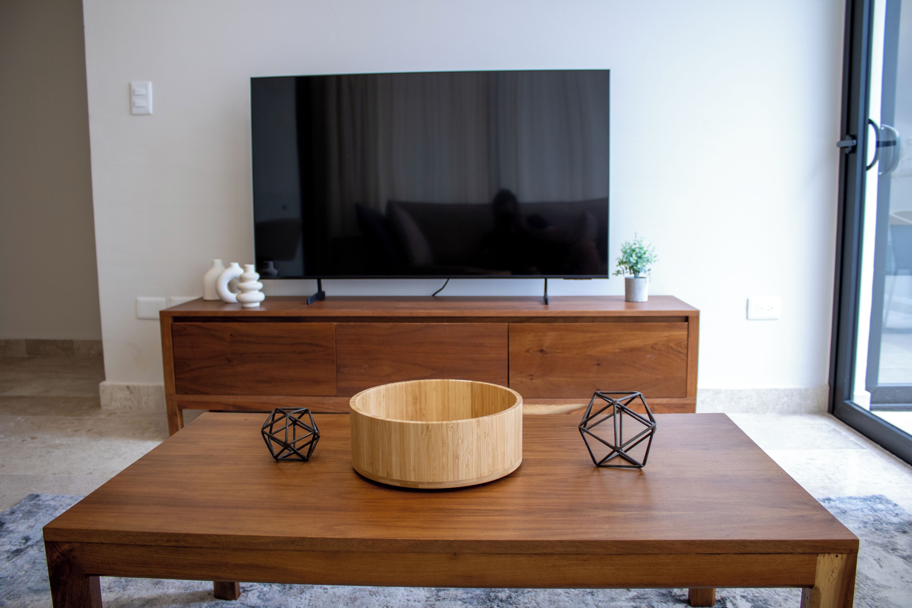 A modern living room with a wooden coffee table, a television on a wooden cabinet, and decorative items.