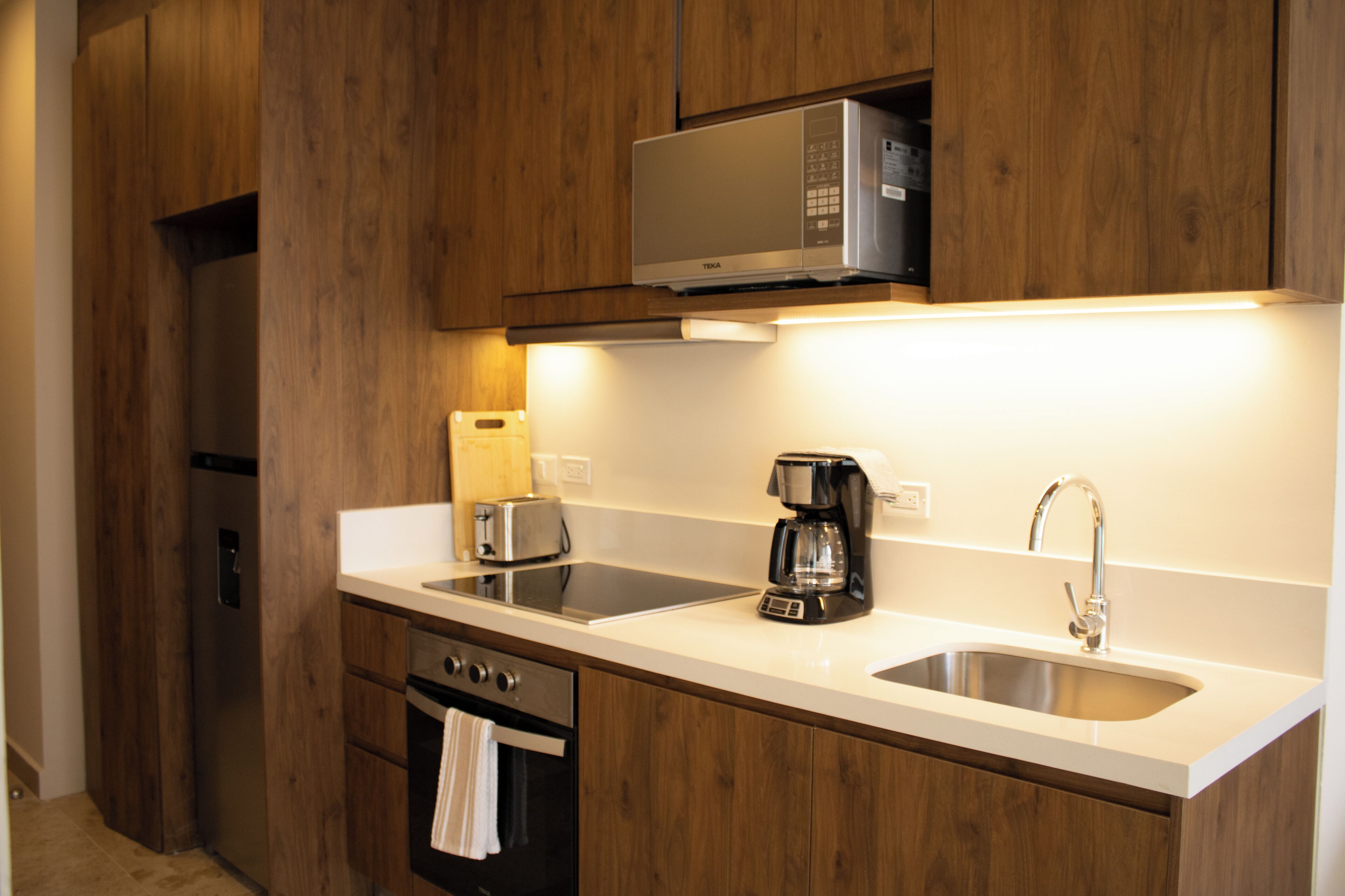 Eine moderne Küche mit Holzausstattung, einem Edelstahlkühlschrank, einer Mikrowelle, einem Toaster und einer Kaffeemaschine.