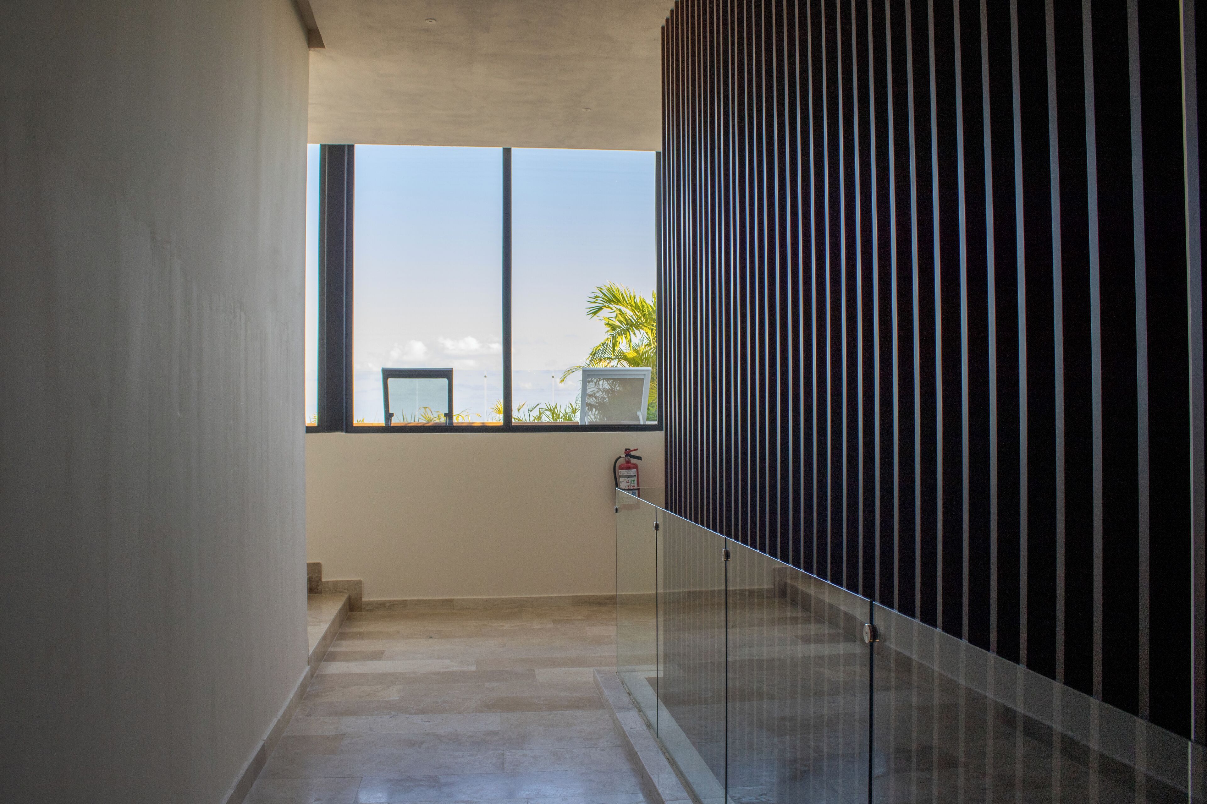 A corridor with a glass railing, a fire extinguisher, and a view of the outdoors.