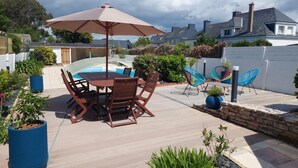 A patio with a table and chairs, a pool, and a white fence. - Les Sternes - ETEL - Gîte (ETEL)