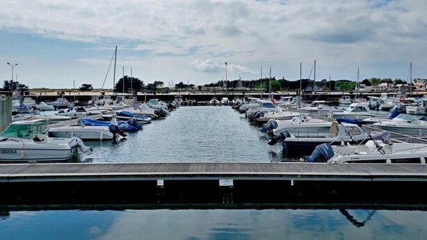 A marina with numerous boats docked along a calm waterway, surrounded by a small town with buildings and trees in the background. - Les Sternes - ETEL - Gîte (ETEL)