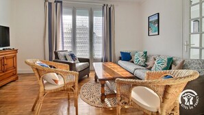 A cozy living room with wicker furniture, a wooden coffee table, and a sofa with patterned cushions. - Les Sternes - ETEL - Gîte (ETEL)