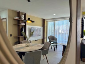 A modern living room with a round dining table, grey chairs, a sofa, and a large window with curtains. - Near the beach in the marina with beautiful views (Mazatlán)