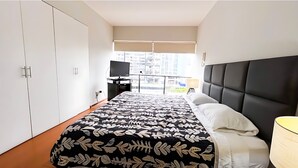 Une chambre à coucher comprenant un lit, une télévision, un bureau et une fenêtre donnant sur la ville.