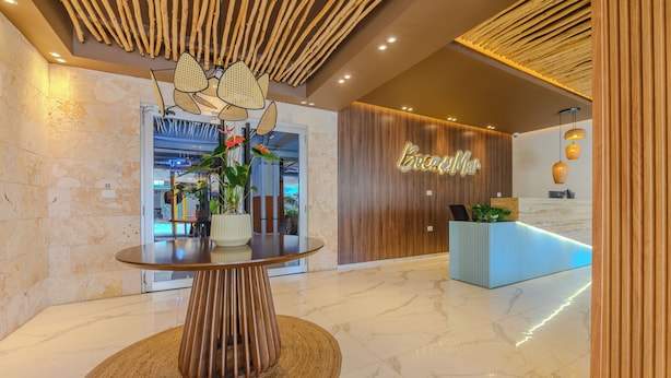 A reception area with a modern reception desk, a round table with a woven base, and a wooden ceiling design. - Apartamento a pasos de la playa  (Boca Chica)