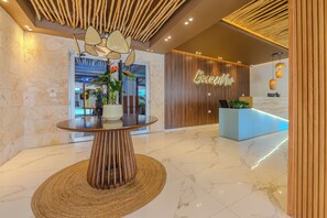 A reception area with a modern reception desk, a round table with a woven base, and a wooden ceiling design. - Apartamento a pasos de la playa  (Boca Chica)