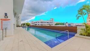 A swimming pool with a tiled deck, a signboard, and a building in the background. - Apartamento a pasos de la playa  (Boca Chica)