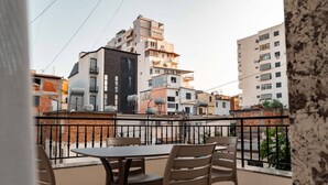 Un balcó amb taula i cadires, amb vista a una zona residencial amb edificis d'altes plantes.