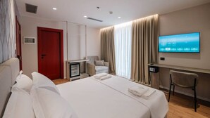 Habitació d'hotel amb un llit gran, escriptori amb televisió de pantalla plana, una cadira, armari i taula petita.