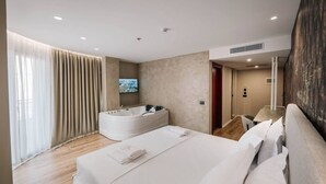 Ein modernes Hotelzimmer mit einem großen Bett, einem separaten Badezimmer mit Whirlwanne und einem flachbildfernseher an der Wand.