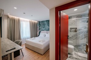 Ett modernt hotellrum med en säng, ett skrivbord och en duschhörna.