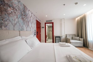 A hotel room with a large bed, a chair, a desk, and a bathroom visible through an open door. - Ermes Deluxe Double Room With Sofa Bed (Durrës)