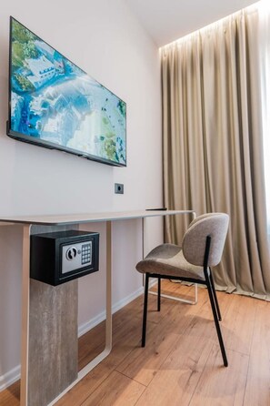 A modern room with a desk, a chair, a painting, and a window with curtains. - Ermes Deluxe Triple Room (Durrës)