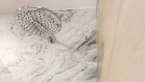 Ett badrum med en vägg av marmor, ett duschmunstycke, en handhållen dusch och en flaska schampo på väggen.