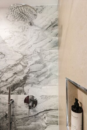 A bathroom with a marble wall, a showerhead, a handheld shower, and a bottle of shampoo on the wall. - Ermes Deluxe Triple Room (Durrës)