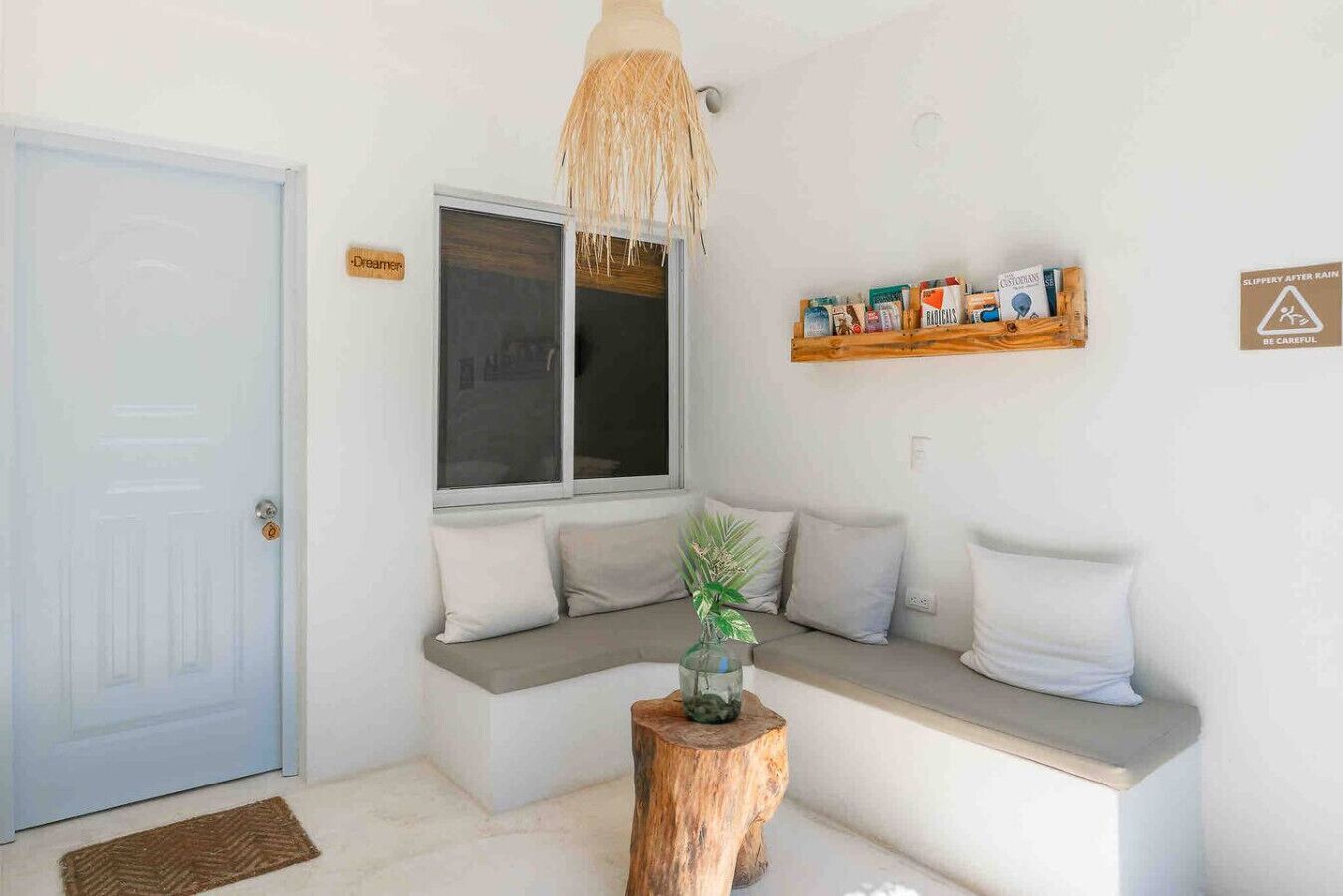 A cozy room with a built-in bench seating area, a wooden stool, a hanging light fixture, and a shelf with books and a sign indicating a wet floor.