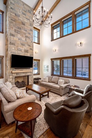 A spacious living room with a stone fireplace, large windows, and modern furniture. - Brand new, 5BR home with private shuttle and concierge (Steamboat Springs)