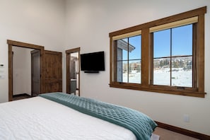 A bedroom with a bed, a TV mounted on the wall, and a window with a view of a snowy landscape. - Beautiful 3BR retreat in Steamboat Springs with mountain views. (Steamboat Springs)