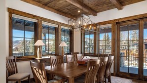 A dining area with a wooden table and chairs, large windows, and a chandelier. - Brand New! 8BR home, private shuttle and concierge (Steamboat Springs)