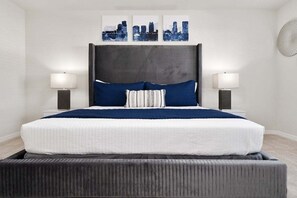 Ein modernes Schlafzimmer mit einem großen Bett, zwei Nachttischlampen und drei abstrakten Wandbildern.