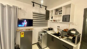 A compact kitchen with a washing machine, a microwave, and a TV mounted on the wall. - Serene 1-bedroom studio with AC in vibrant Accra (Accra)