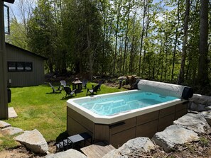 Un bain à remous dans un jardin, avec une terrasse en bois, des chaises et un abri de jardin.