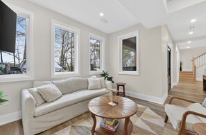 Ein modernes Wohnzimmer mit einer Couch, einem runden Couchtisch und großen Fenstern.