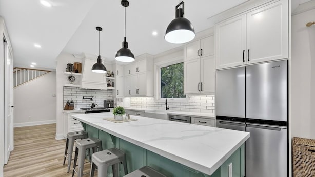Une cuisine moderne avec des meubles blancs, un réfrigérateur en acier inoxydable et un grand îlot central doté de tabourets de bar.