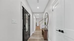 Un couloir aux murs blancs, avec un plancher en bois et un escalier en arrière-plan.