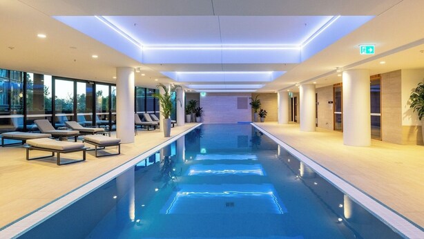 A modern indoor swimming pool with lounge chairs and potted plants. - Modern and Cozy 1-Bedroom Apartment in Phillip (Phillip)