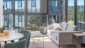 A modern interior with a large window, a grey sofa, a small table, and a green chair. - Modern and Cozy 1-Bedroom Apartment in Phillip (Phillip)