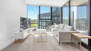 A modern living room with a large window, a flat-screen TV, a sofa, and a coffee table. - Modern and Cozy 1-Bedroom Apartment in Phillip (Phillip)