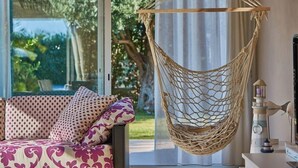 En hängmatta som stol, en mönstrad soffa och en dekorativ modell av ett fyrtorn i ett rum med ett stort fönster.