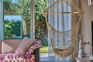 A hammock chair, a patterned sofa, and a decorative lighthouse model in a room with a large window. - Villa Marbella, a short walk from the beach (Marina di Ragusa)