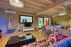 A living room with a sofa, coffee table, hanging chair, TV, and dining area with chairs and table. - Villa Marbella, a short walk from the beach (Marina di Ragusa)