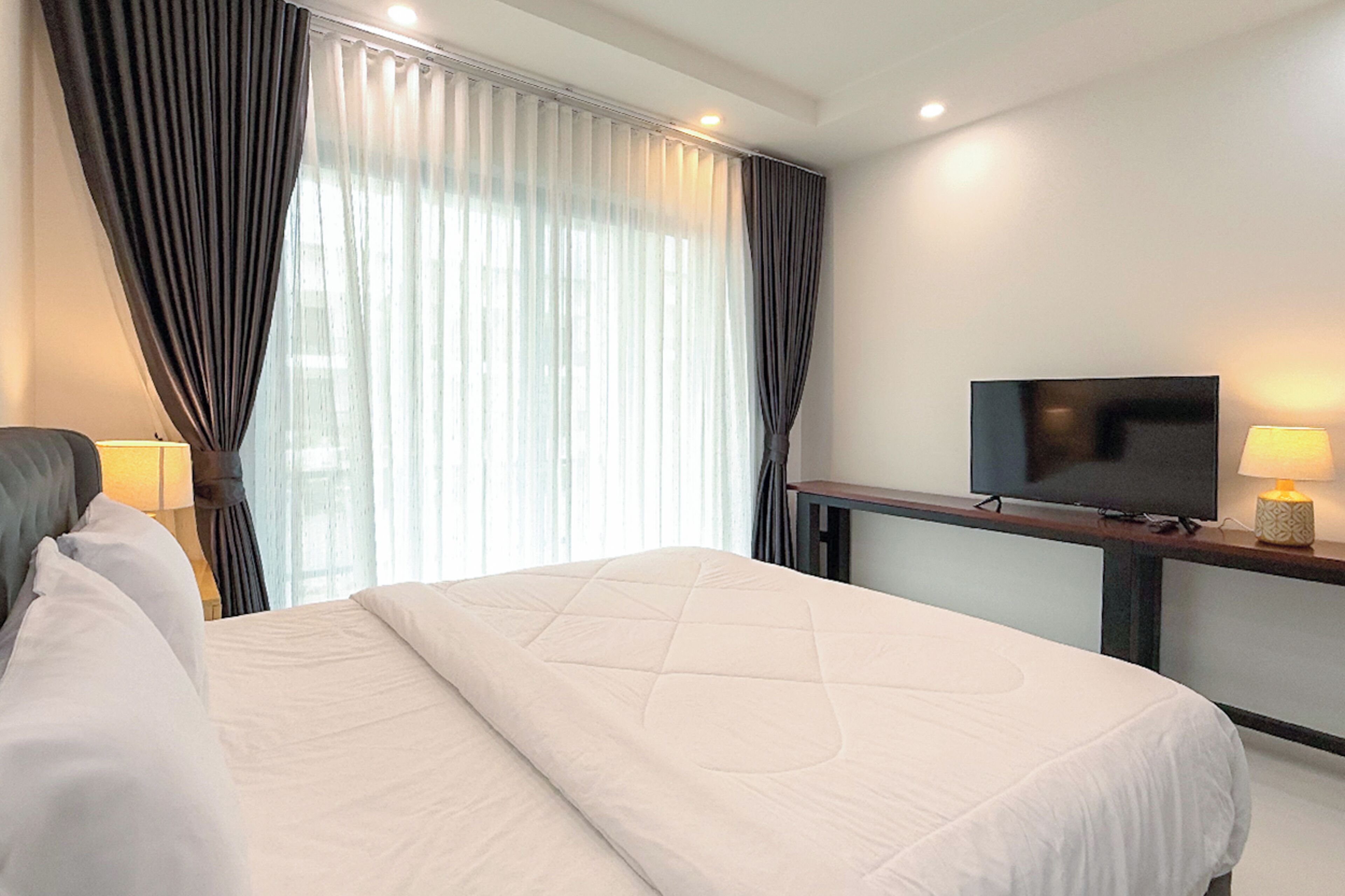 Een hotelkamer met een bed, een televisie op een standaard, een bureau met een lamp en een raam met gordijnen.