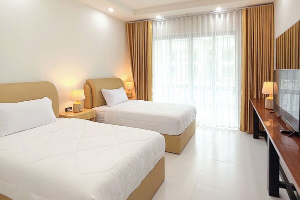 A hotel room with two beds, a TV, and a large window with curtains.