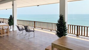 Un espace extérieur abrité, aménagé avec des tables et des chaises en bois, offrant une vue sur la mer et agrémenté de deux sapins de Noël.