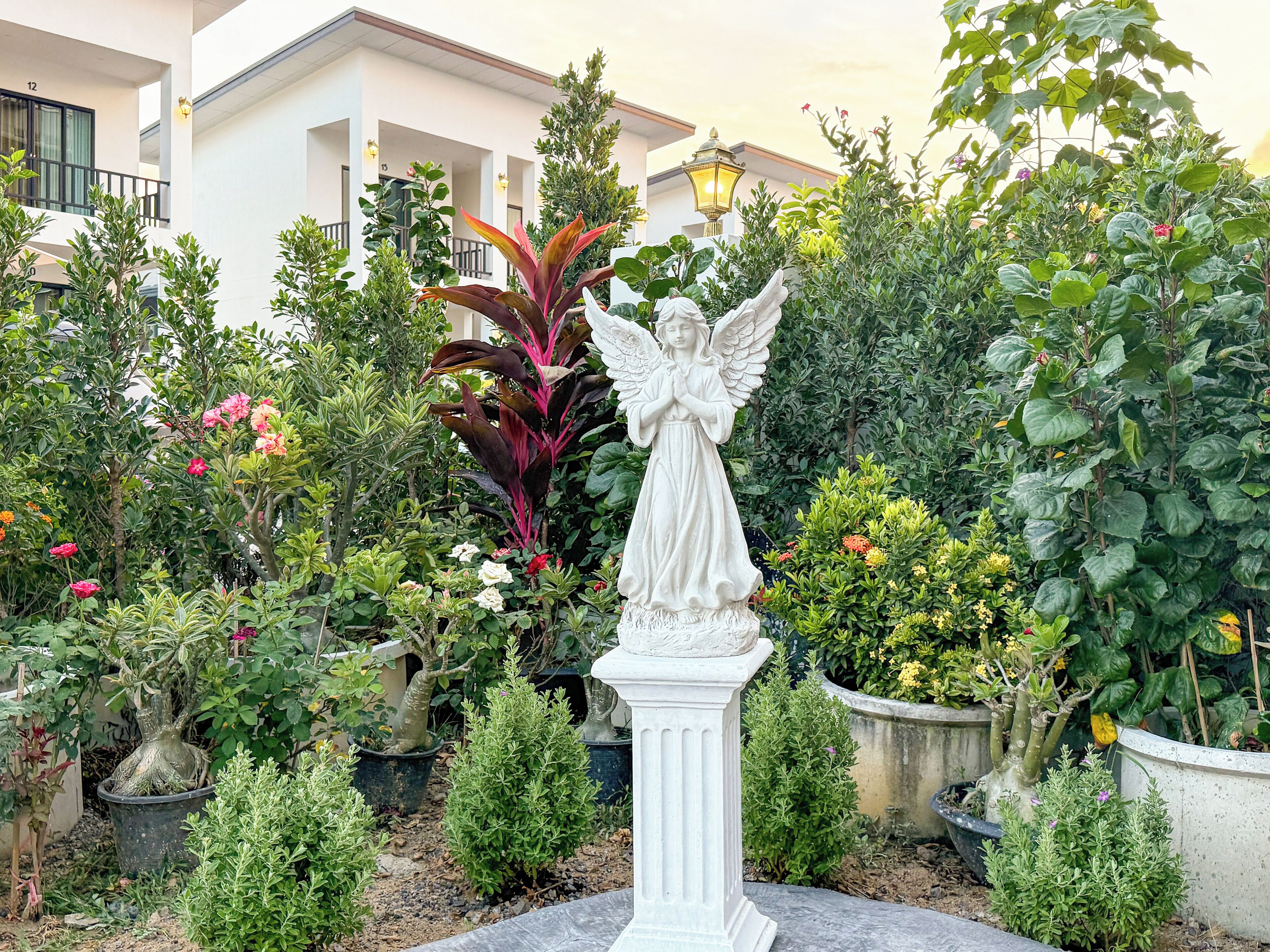 A garden with a white angel statue, various potted plants, and a building in the background.