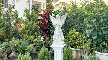 A garden with a white angel statue, various potted plants, and a building in the background.