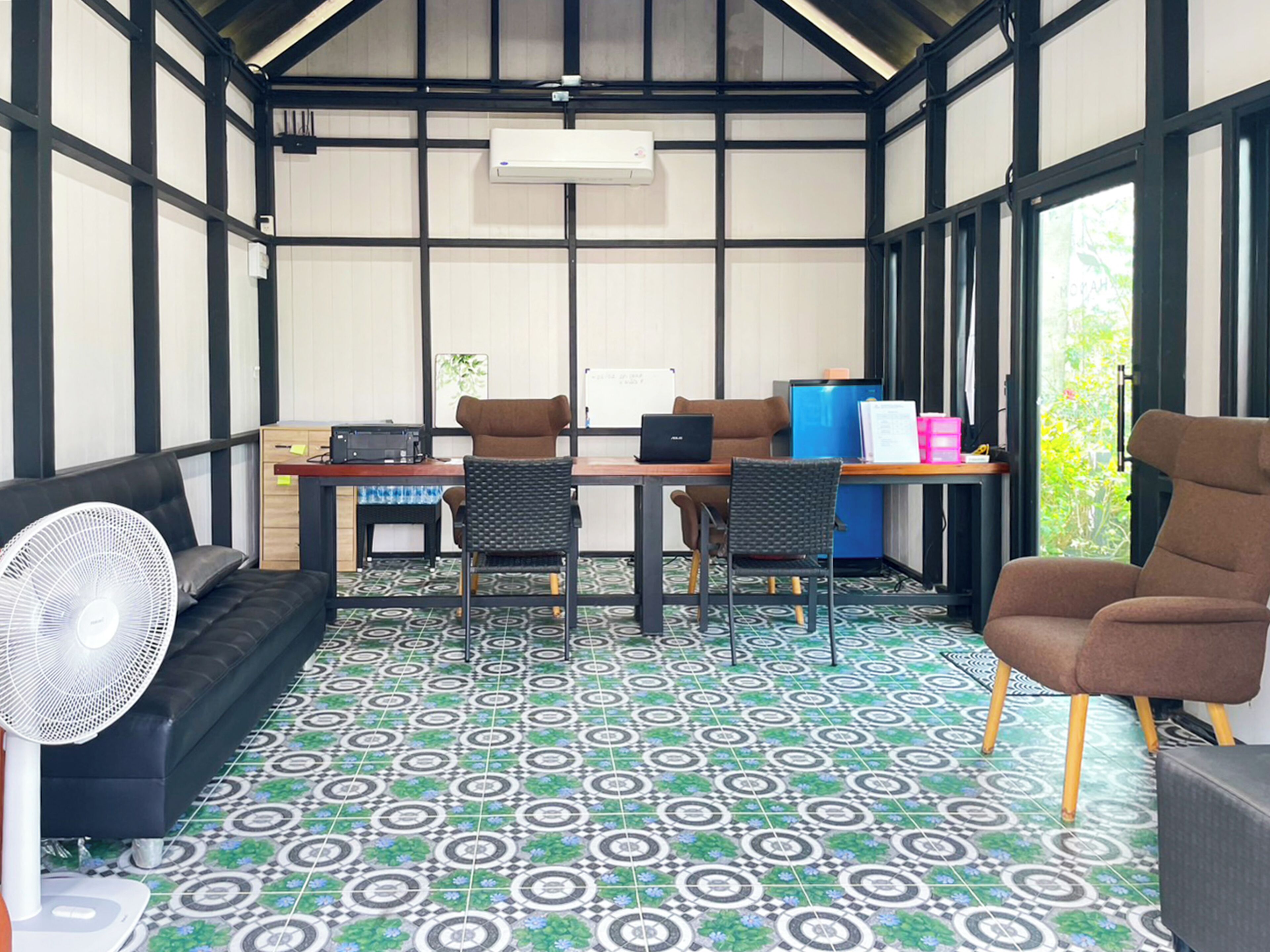 Una habitación con escritorio, dos sillas, sofá y ventilador.