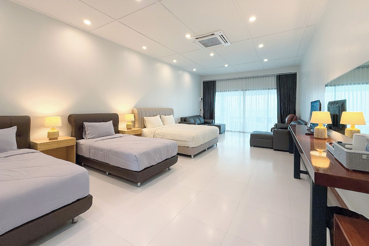 A hotel room with three beds, a desk with a computer, and a large window with curtains.
