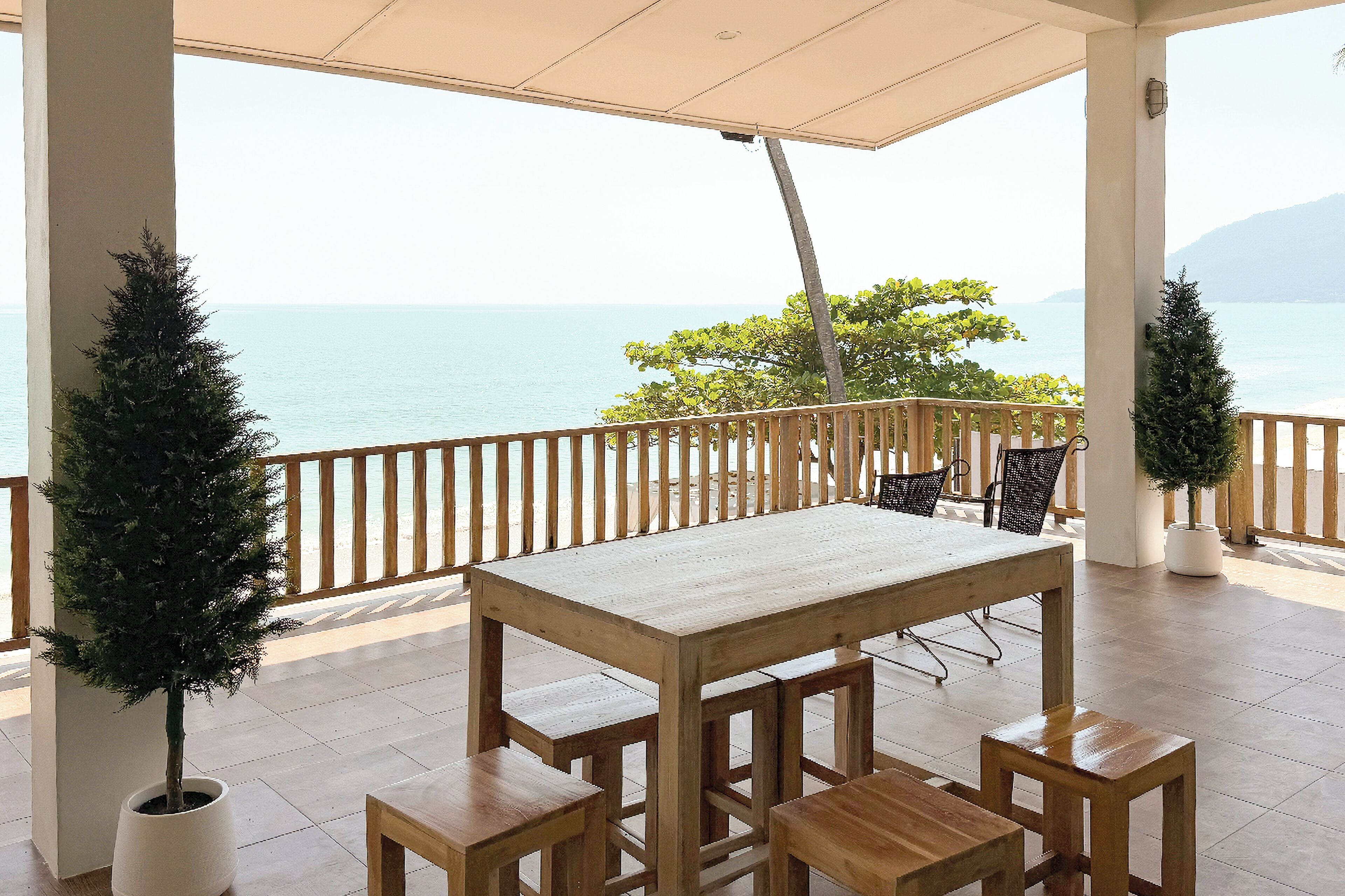 Una mesa y sillas de madera en una terraza con vistas al mar y a las montañas.
