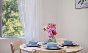 A dining table with blue plates and a vase of pink flowers. - KozyGuru | Macquarie Park | Sunny Apt near Metro (Macquarie Park)